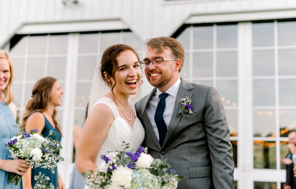 groom smiling at bride on behind barn glass doors at Castle Hill Cider